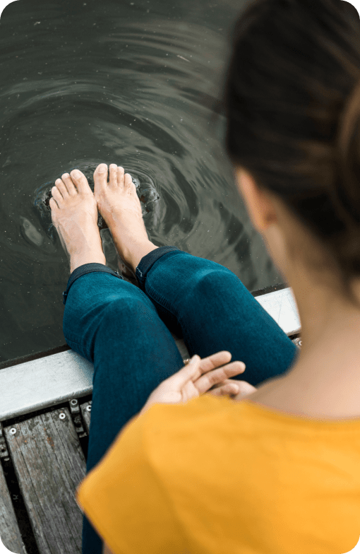 Mujer que se mira los pies mientras está sentada en un muelle con los pies en el agua.