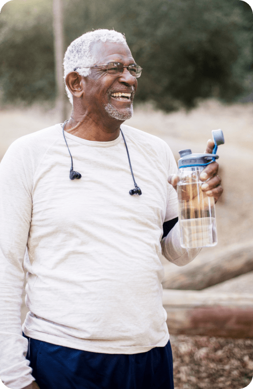 Hombre sonriente que sostiene una botella de agua mientras camina al aire libre.